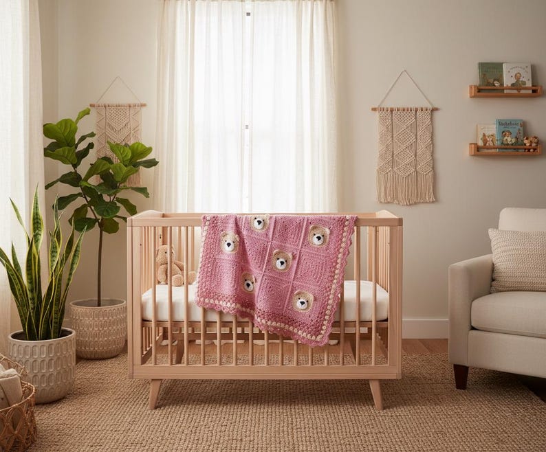 May include: A light pink crocheted baby blanket featuring a repeating square pattern with integrated plush bear faces. The blanket has a decorative scalloped border and is draped over the side of a light-toned wooden crib with vertical slats.