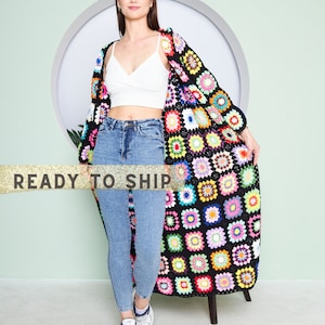 May include: A long, colorful crochet cardigan with a floral pattern. The cardigan features a black base with vibrant squares of pink, yellow, blue, and green. The text "READY TO SHIP" is across the image.