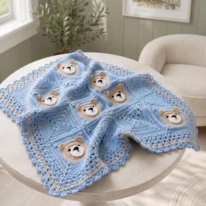 May include: A square crochet blanket featuring a repeating pattern of light blue squares and tan bear faces with white muzzles and black noses. The blanket has a decorative scalloped border in light blue and tan, constructed from yarn.
