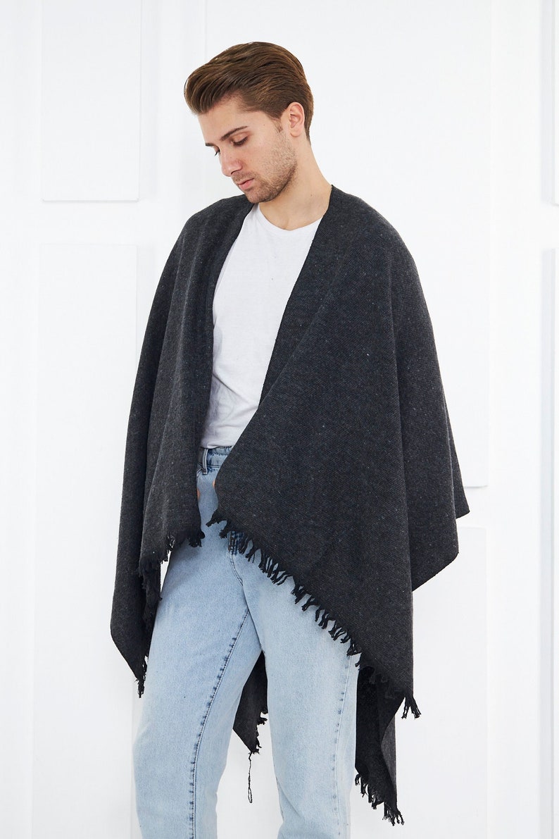 May include: A charcoal gray shawl with fringed edges. The shawl is draped over a person wearing a white t-shirt and light blue jeans.