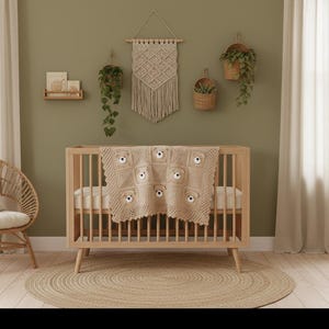 May include: A light beige crochet baby blanket featuring a repeating pattern of square motifs, each centered with a small, three-dimensional stuffed bear face with dark eyes and a nose, draped over a wooden crib with vertical slats and tapered legs.