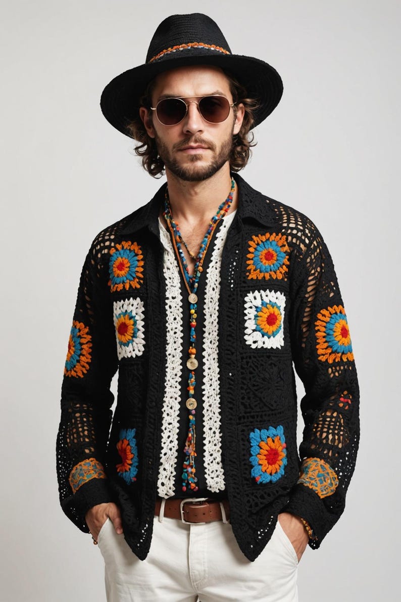 May include: A black crochet jacket with colourful square patterns, worn over a white shirt with a beaded necklace. The person is wearing a black hat and sunglasses.