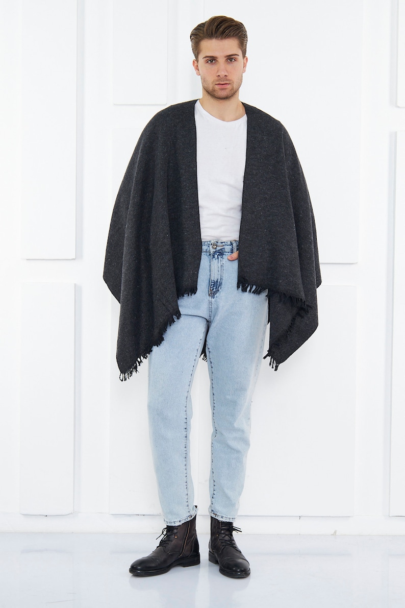 May include: A person wearing a dark gray shawl with a fringe trim over a white t-shirt and light blue jeans. They are wearing black leather boots.
