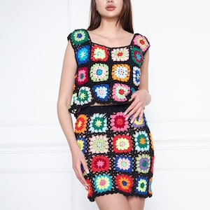 Puede incluir: Un conjunto de top y falda de crochet de colores. El top y la falda están hechos de hilo negro con cuadrados coloridos que presentan un patrón floral.