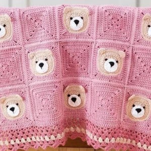May include: A pink crochet blanket featuring a repeating pattern of square blocks. Several blocks contain a beige bear face with a white muzzle and black nose. The blanket is finished with a decorative scalloped border in pink and cream yarn.