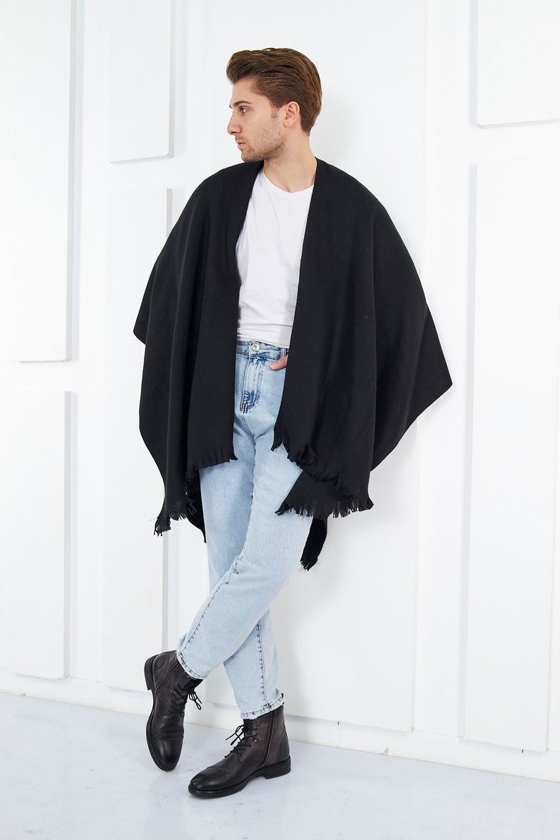 May include: A black fringed shawl worn over a white t-shirt and light blue jeans. The person is wearing black leather boots.