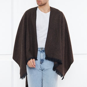 May include: A brown and black fringed shawl with a black trim. The shawl is draped over a person wearing a white t-shirt and blue jeans.