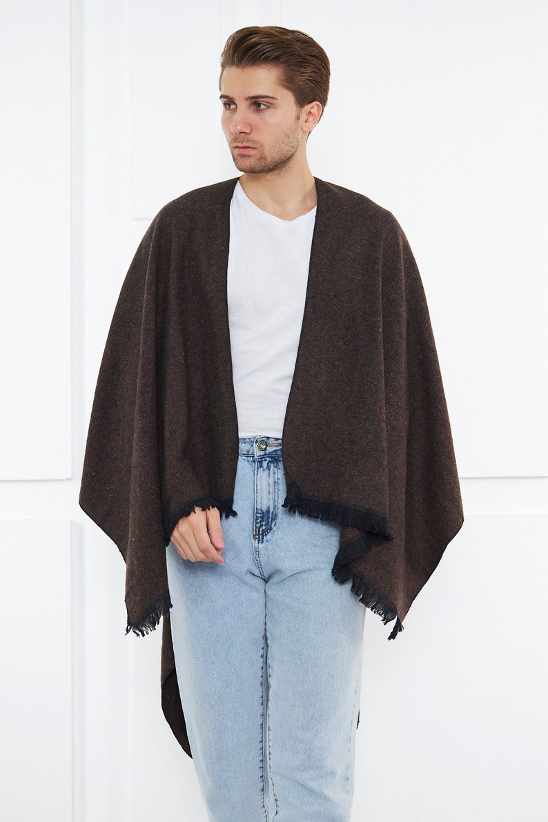 May include: A brown and black fringed shawl with a black trim. The shawl is draped over a person wearing a white t-shirt and blue jeans.