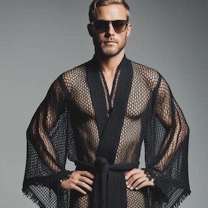 May include: A black mesh robe with a tie waist and wide sleeves. The robe is worn open, revealing the chest. The model is wearing sunglasses and has short, light-colored hair.