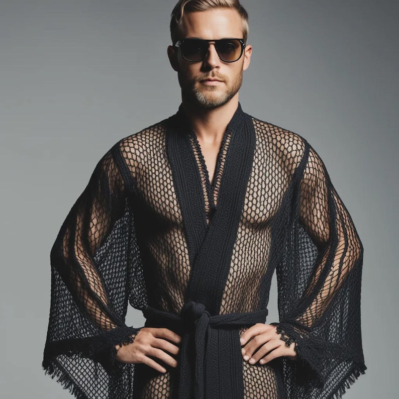 May include: A black mesh robe with a tie waist and wide sleeves. The robe is worn open, revealing the chest. The model is wearing sunglasses and has short, light-colored hair.