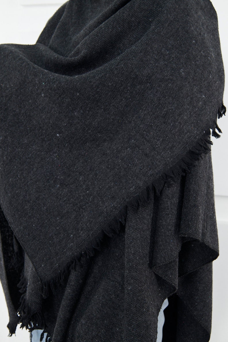 May include: A dark gray fringed scarf made of a soft, textured fabric.