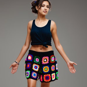 May include: Black crochet shorts with colorful square patterns. The shorts feature a high waist and a vibrant mix of red, yellow, green, blue, and pink squares. The model is wearing a dark blue tank top.