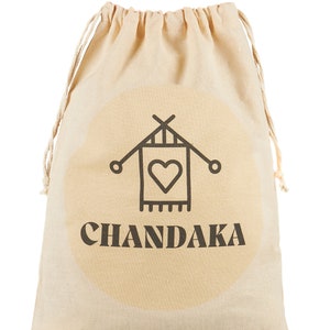 May include: Beige drawstring bag with a circular design and the word "CHANDAKA" printed in dark brown. The bag features a black graphic of a house with a heart inside. The drawstring is a light beige color.