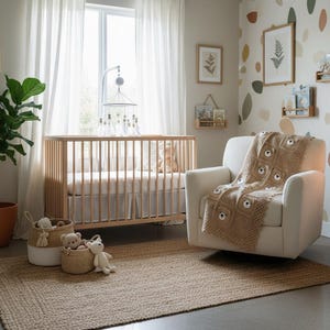 May include: A beige knit blanket featuring a repeating square pattern with small bear faces, draped over a cream-colored upholstered armchair. The blanket has a textured, crocheted appearance with light brown yarn and white accents on the bear faces.
