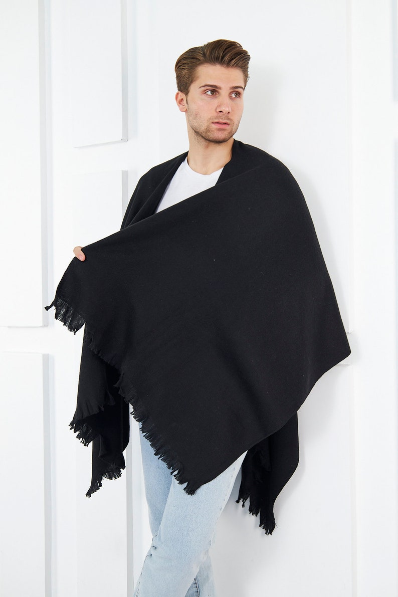 May include: A black fringed shawl draped over a person's shoulders. The shawl is made of a soft, textured fabric and has a simple, elegant design.