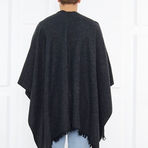 May include: A dark gray poncho with a fringed edge. The poncho is made of a soft, textured fabric.