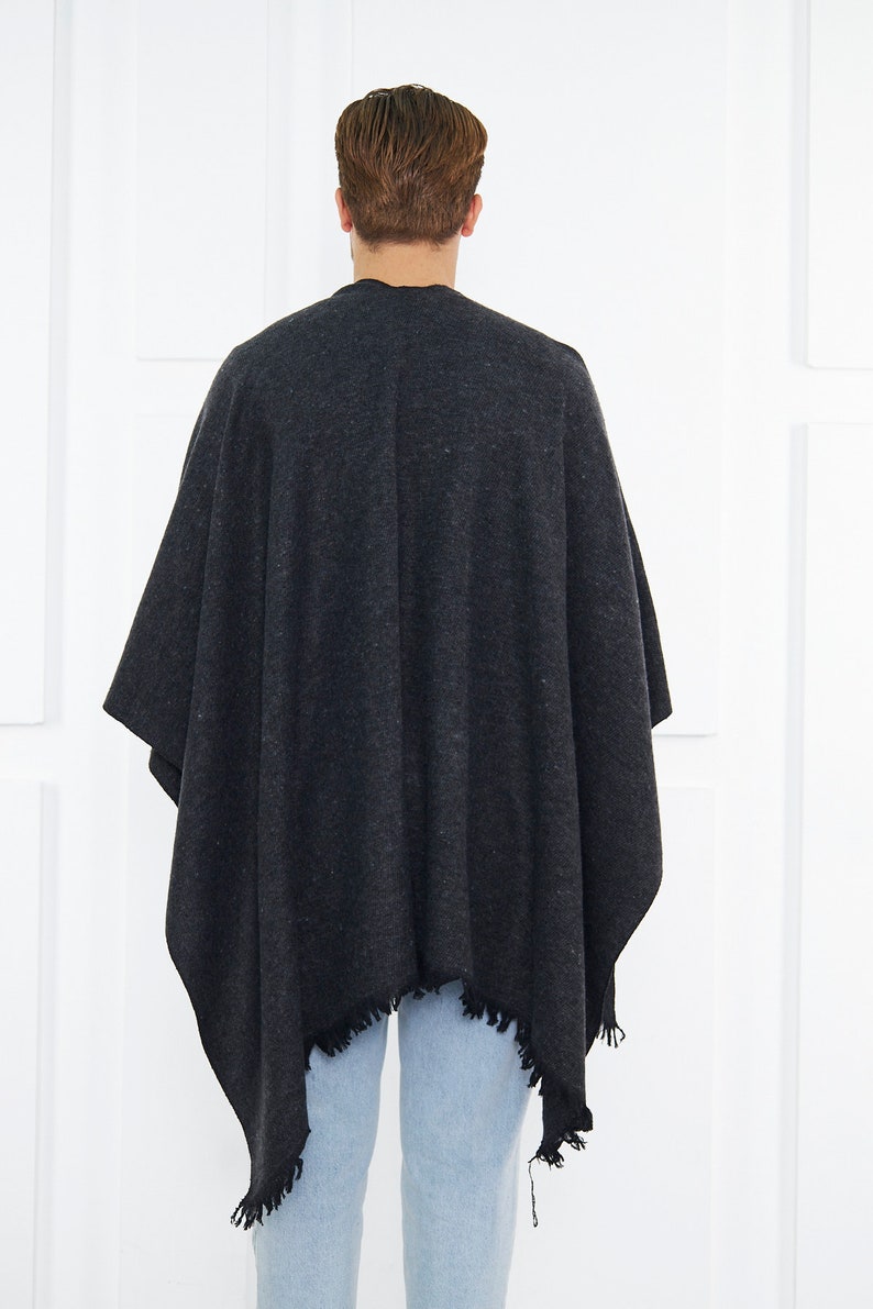 May include: A dark gray poncho with a fringed edge. The poncho is made of a soft, textured fabric.