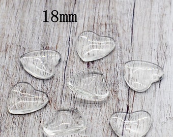 May include: Six clear glass heart-shaped cabochons, each measuring 18mm in diameter, are arranged on a light wood surface. 18mm