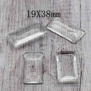 May include: Four clear glass rectangular cabochons, each measuring 19mm x 38mm, are arranged on a light wood surface.