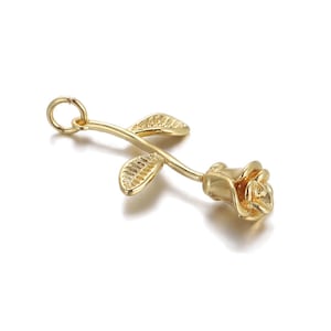May include: A gold-colored rose pendant with a stem and two leaves. The rose is in full bloom, and the leaves have detailed veining. The pendant has a small loop at the top for attaching to a chain or other jewelry.