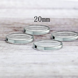 May include: Four clear glass circles, each measuring 20mm in diameter, are arranged on a light wood surface.  The circles are slightly raised from the surface, giving them a 3D effect.