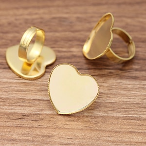 May include: Three gold heart-shaped ring blanks with a smooth, shiny finish. The rings are made of metal and have a beveled edge.