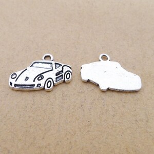 May include: Two silver-colored car charms. One charm is a detailed side view of a car with wheels, windows, and headlights. The other charm is a simplified outline of a car. Both charms have a small loop at the top for attaching to a necklace or bracelet.