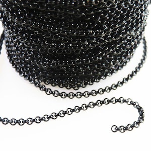 May include: A spool of black chain with small, round links. The chain is tightly wound on the spool, with a length of chain extending out. The chain has a shiny, reflective surface.
