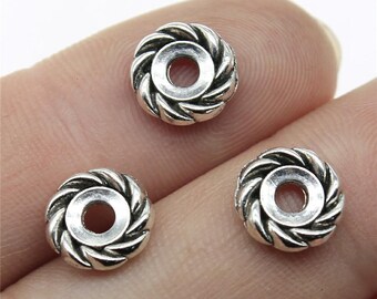 May include: Three silver-colored, round beads with a spiral design around a central hole. The beads are small, with a detailed, textured surface. The beads are likely for jewelry making or crafts.