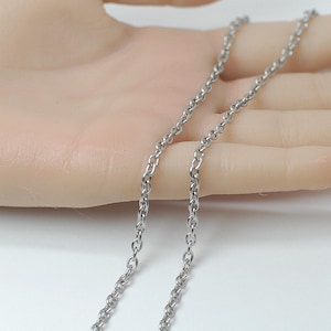 May include: A silver-colored chain necklace with a delicate, linked design. The chain is displayed against a neutral background, highlighting its simple elegance. The necklace appears to be made of metal and is suitable for everyday wear.