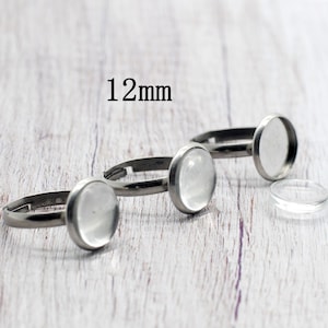May include: Three silver adjustable rings with 12mm clear glass cabochons. The rings are on a white wooden surface.
