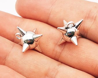 May include: Two silver-colored, star-shaped charms with pointed spikes. Each charm has a small loop at the top for attaching to jewelry. The charms are displayed against a neutral background.