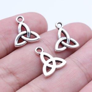May include: Three silver-colored Celtic knot charms. Each charm features a triquetra design with a loop at the top for attaching to jewelry. The charms are made of a shiny metal and are displayed against a neutral background.