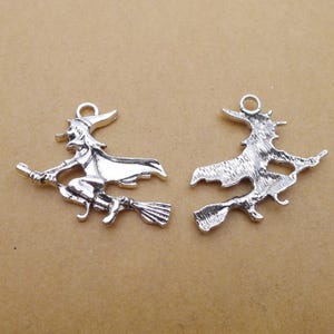 May include: Two silver-colored witch charms, each depicting a witch riding a broom. The charms have a loop at the top for attaching to jewelry or other crafts. The witch is wearing a hat and cape.