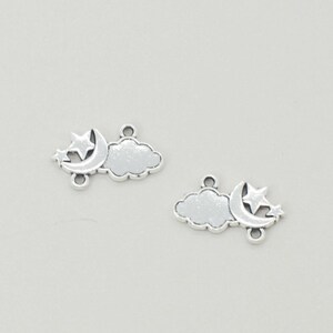 May include: Two silver-colored charms in the shape of a cloud, crescent moon, and star. Each charm has a small loop at the top and bottom for attaching to jewelry. The charms are on a light gray background.