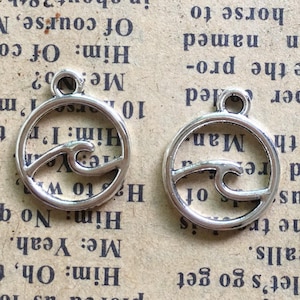 May include: Two silver-colored wave charms. Each charm features a wave design within a circular frame, with a small loop at the top for attaching to jewelry or other crafts. The charms are made of metal.