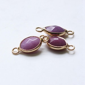 May include: Three purple gemstone connectors with gold-coloured metal frames and small loops on each end. The gemstones have a faceted surface, and the connectors are arranged on a white background. Suitable for jewellery making.