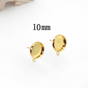 May include: Two gold-toned earring settings with a 10 mm round bezel and a jump ring. The earring settings are on a white background.