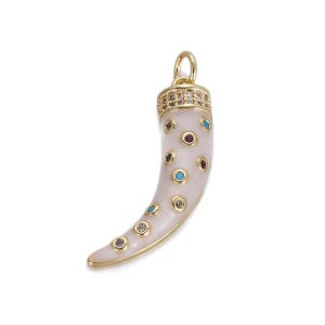 May include: A gold-colored pendant in the shape of a horn, with a cream-colored body and colorful gemstone accents. The top of the horn is embellished with small, clear gemstones. The pendant has a loop for a chain.