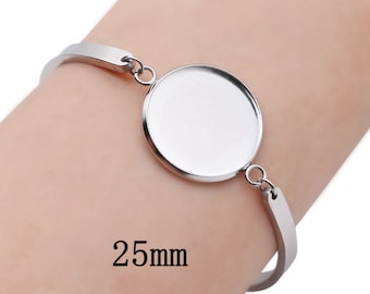 May include: A silver-toned bracelet with a circular bezel, designed to hold a 25mm insert. The bracelet has a simple, elegant design, perfect for customization. The text "25mm" is displayed on the image.