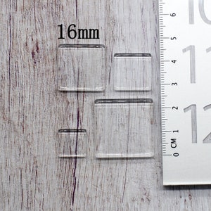 May include: Four clear, square glass pieces of varying sizes are displayed. The largest piece is approximately 16mm. A ruler with both centimeters and inches is positioned next to the glass squares, providing a size reference.