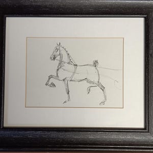 May include: A black and white pencil sketch of a horse in motion. The horse is drawn in a simple, stylized manner, with its legs extended and its head turned to the side. The sketch is framed in a black frame.
