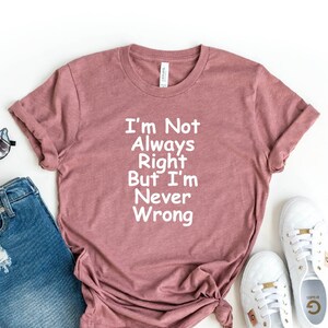 May include: A heather mauve t-shirt with the text "I'm Not Always Right But I'm Never Wrong" in white. The shirt is paired with denim shorts, white sneakers, and sunglasses.