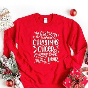 May include: Red Christmas sweatshirt with white text that reads "The best way to spread Christmas cheer is singing loud for all to hear."