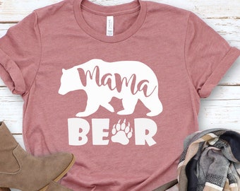 May include: A mauve t-shirt with a white silhouette of a bear and the text "mama bear" with a paw print.