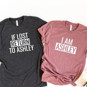 May include: Two t-shirts, one heather dark grey and one heather mauve, with white text. The grey shirt says "IF LOST RETURN TO ASHLEY" and the mauve shirt says "I AM ASHLEY".