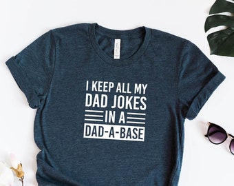 May include: A dark blue t-shirt with the text "I keep all my dad jokes in a dad-a-base" printed in white. The shirt is made of a soft, comfortable material and is perfect for everyday wear.