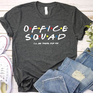 May include: A dark gray t-shirt with the text "OFFICE SQUAD" in white with colorful dots. The text "I'LL BE THERE FOR YOU" is printed below in smaller white text.