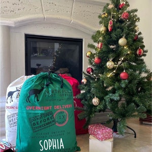 May include: Green and white Christmas gift bag with a reindeer design and the text "North Pole Post Office" and "Overnight Delivery". The bag has a red and white label that says "Do Not Open Before 25 December". The bag is personalized with the name "Sophia".