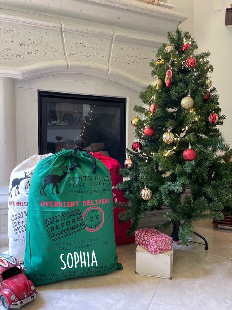 May include: Green and white Christmas gift bag with a reindeer design and the text "North Pole Post Office" and "Overnight Delivery". The bag has a red and white label that says "Do Not Open Before 25 December". The bag is personalized with the name "Sophia".